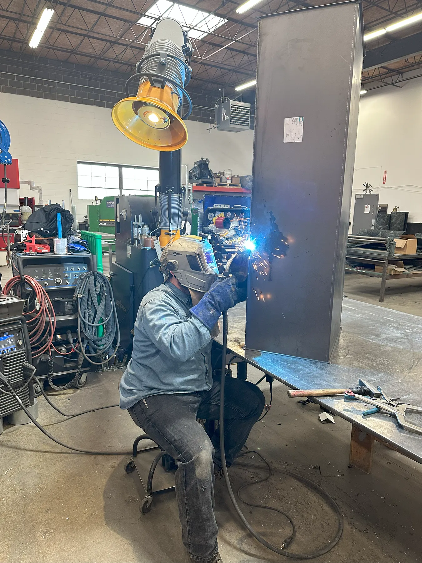 Professional Welding Services in Action A professional welder wearing protective gear performs a precision weld on a large metal beam inside an industrial fabrication shop.